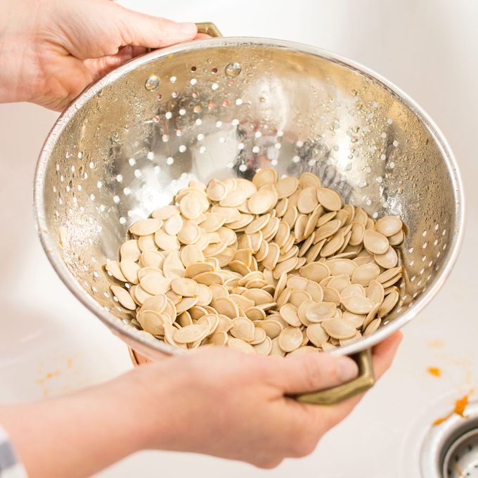 hands rinsing pumpkin seeds in a metal strainer