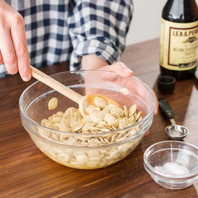 hands mixing pumpkin seeds in a glass bowl