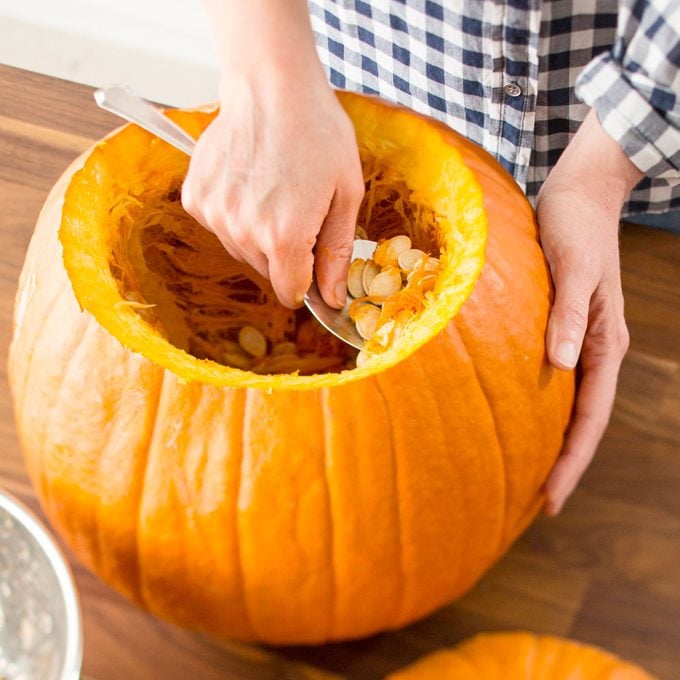 hands scooping the insides out of a large orange pumpkin