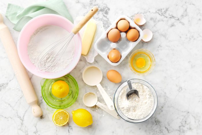 eggs, lemons, butter, and batter in various bowls with a whisk and rolling pin on the side