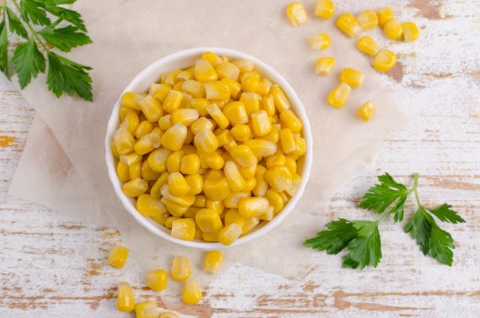 Sweet canned corn in a bowl with parsley to the side on a rustic light colored wooden surface