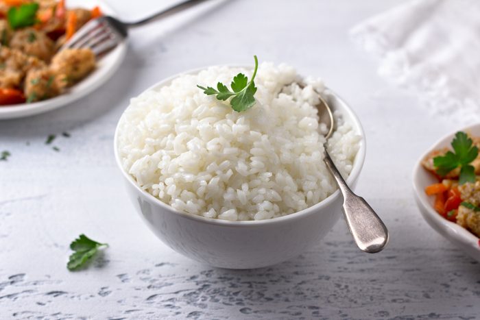 A bowl of cooked rice with a stew of soy meat and vegetables on a light gray background. vegan natural diet food