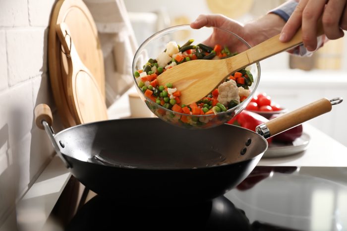 Man pouring mix of frozen vegetables into frying pan, closeup