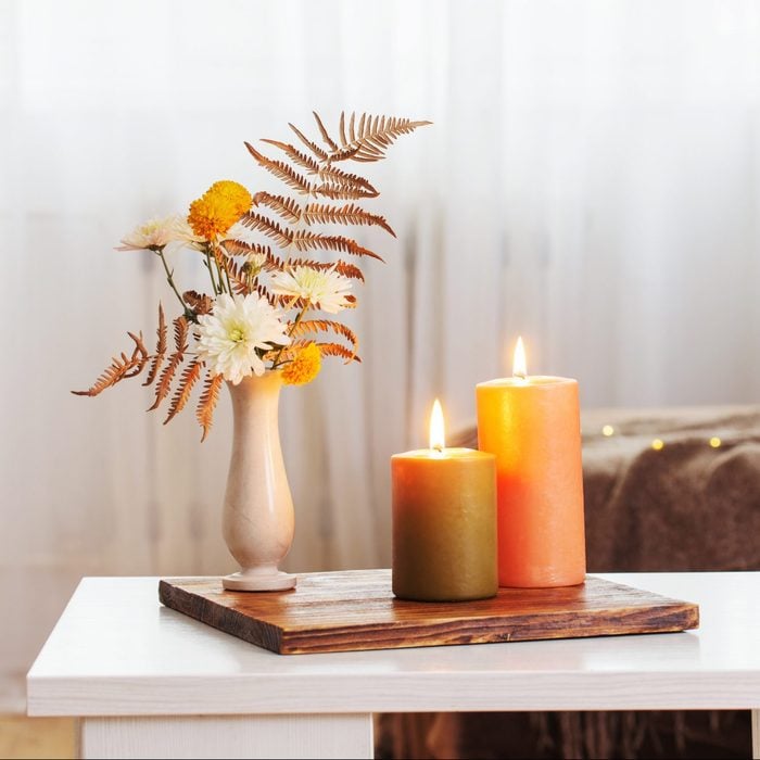 burning candles with autumn decor on white table at home