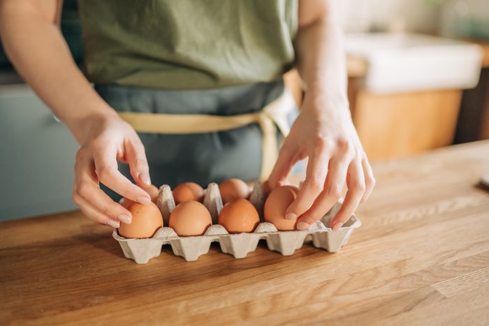 close up of woman's hands with some brown eggs in an egg carton on a kitchen counter