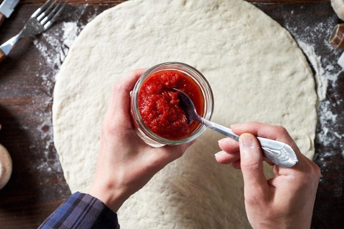 hands with a jar of tomato pasta sauce and pizza dough below