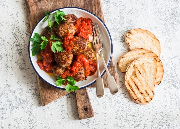Baked meatballs with tomato sauce and herbs on a wooden cutting Board on white background. Top view. Delicious lunch