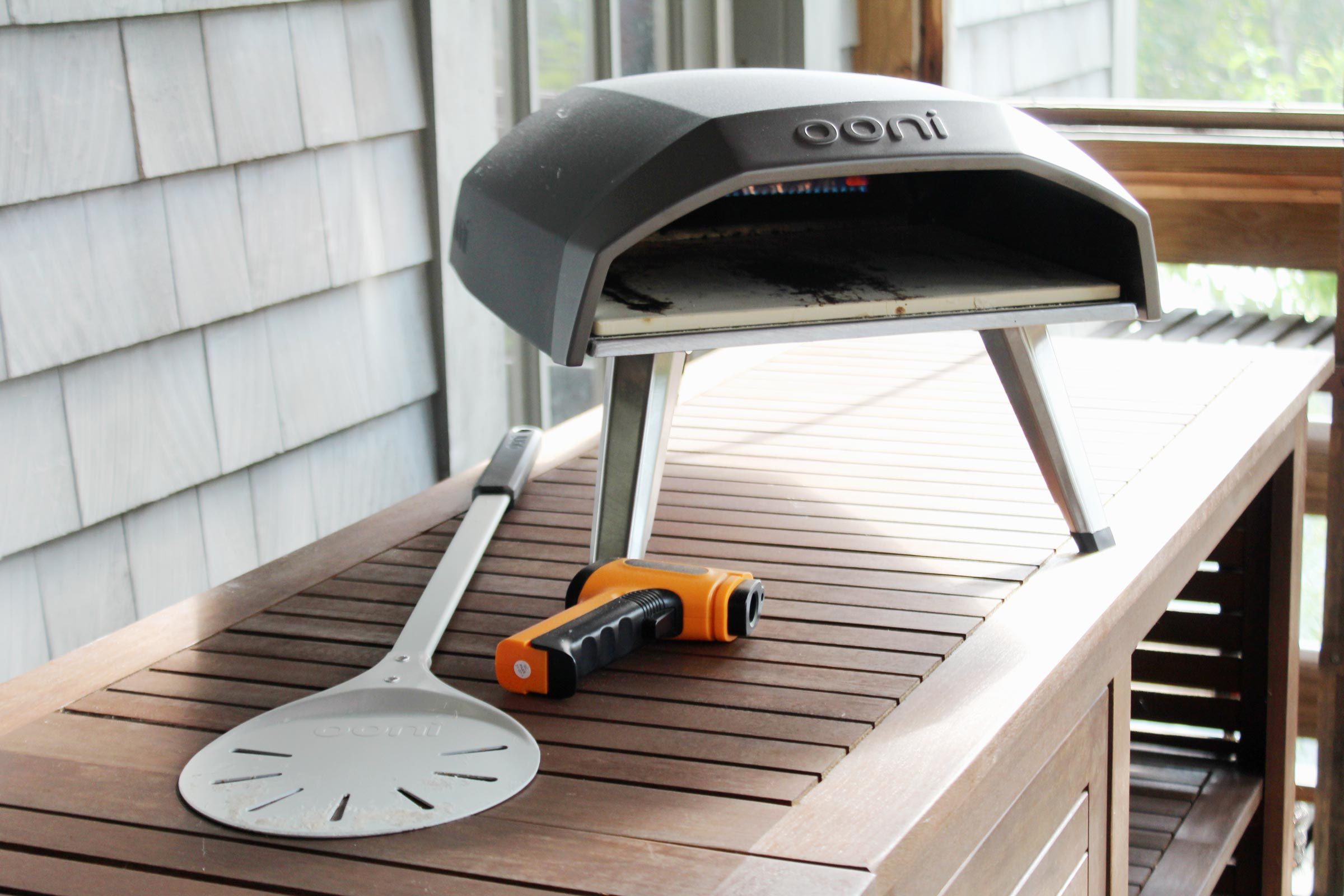 Oonie pizza oven with a pizza peel and thermometer outside on a table