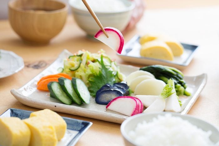 chopsticks picking up a piece of pickled radish from a white plate filled with a variety of other Japanese pickles