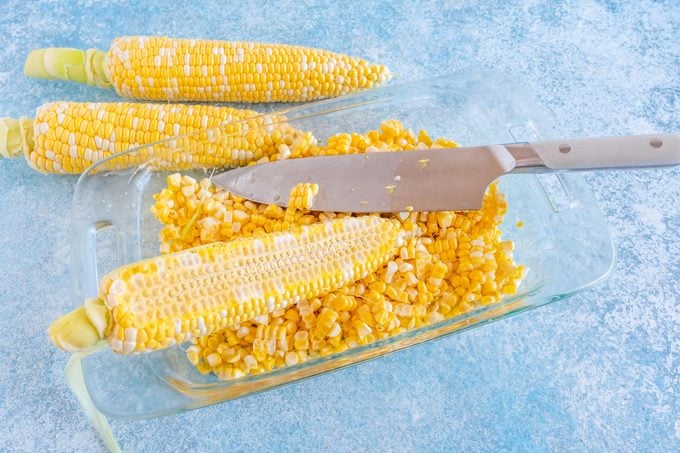 cutting off corn from the cob into a glass casserole dish