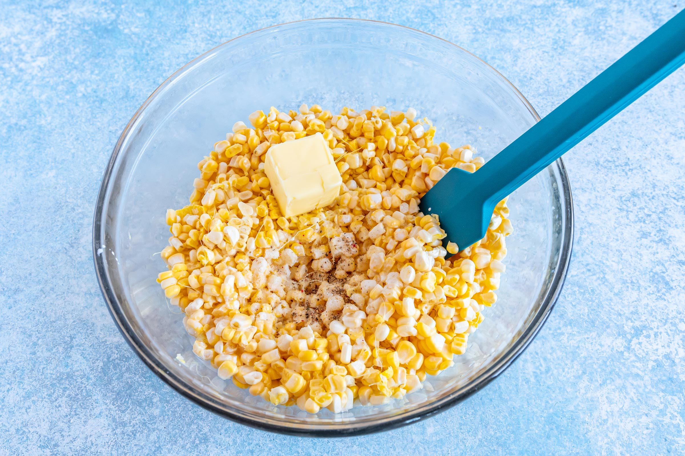mixing corn and ingredients with a teal rubber spatula in a clear glass bowl