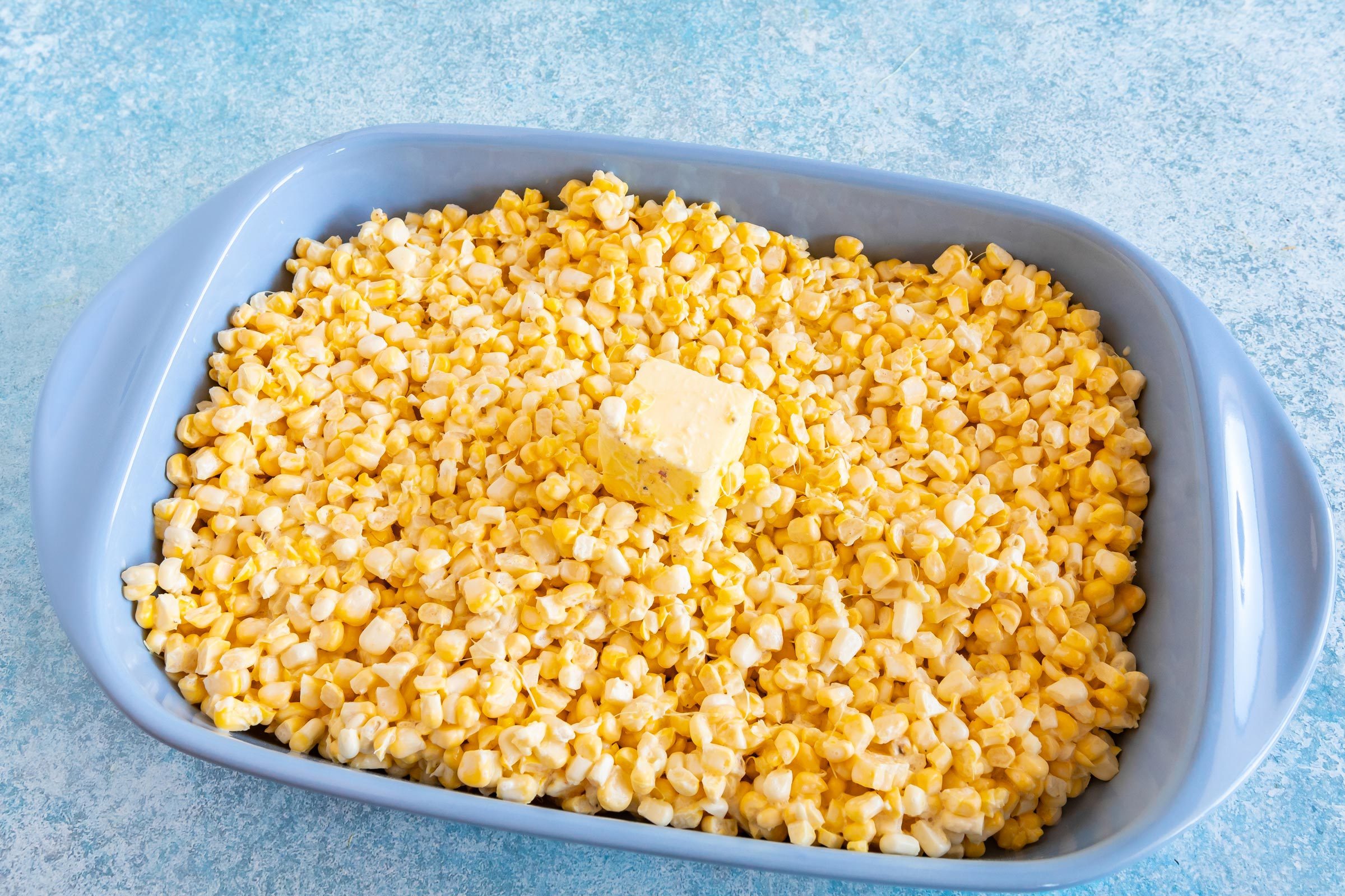 corn casserole in a blue serving dish and a piece of butter on top