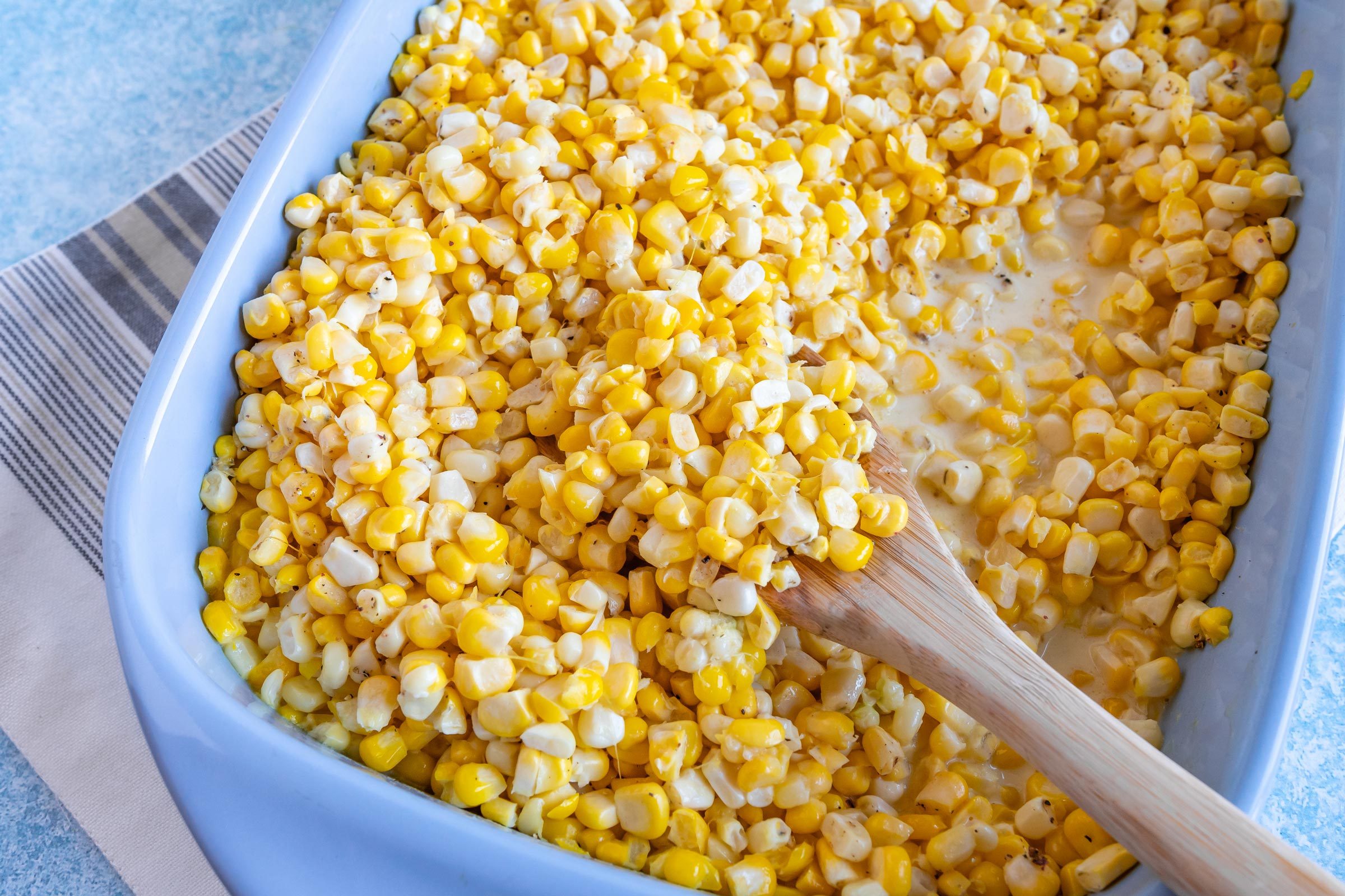 corn casserole in a blue serving dish with a wooden spoon