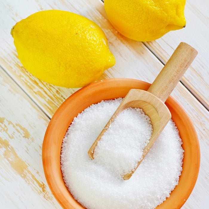 Citric Acid in a bowl And two Lemons on white wood surface