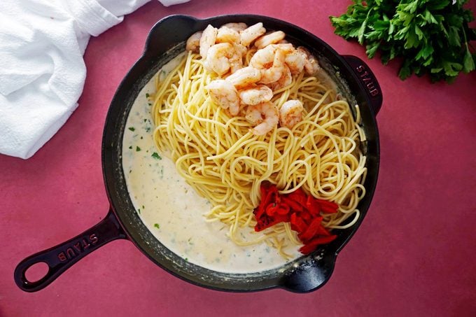 mixing the pasta, shrimp and other ingredients in the cream sauce in a cast iron pan