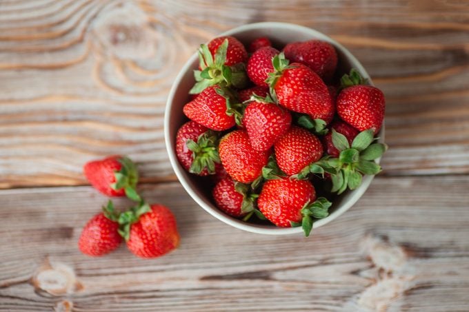 Bowl of ripe strawberries on wooden table - stock photo