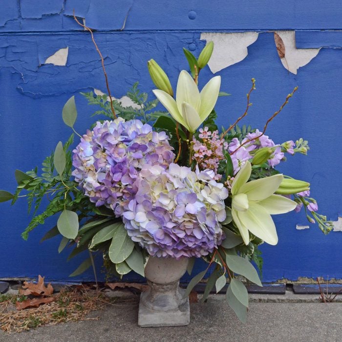 Floral arrangement of purple hydrangeas and lillies on a blue background