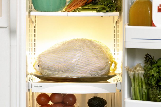 Open refrigerator with frozen turkey on shelf