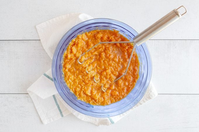 mashed sweet potatoes in a blue glass bowl with a masher