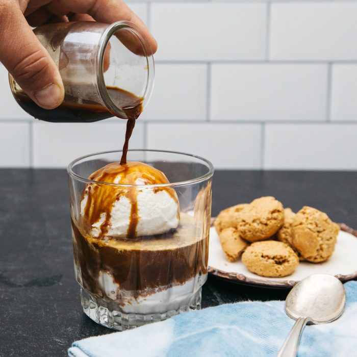hand pouring espresso over ice cream I na cup with a plate of cookies in the background