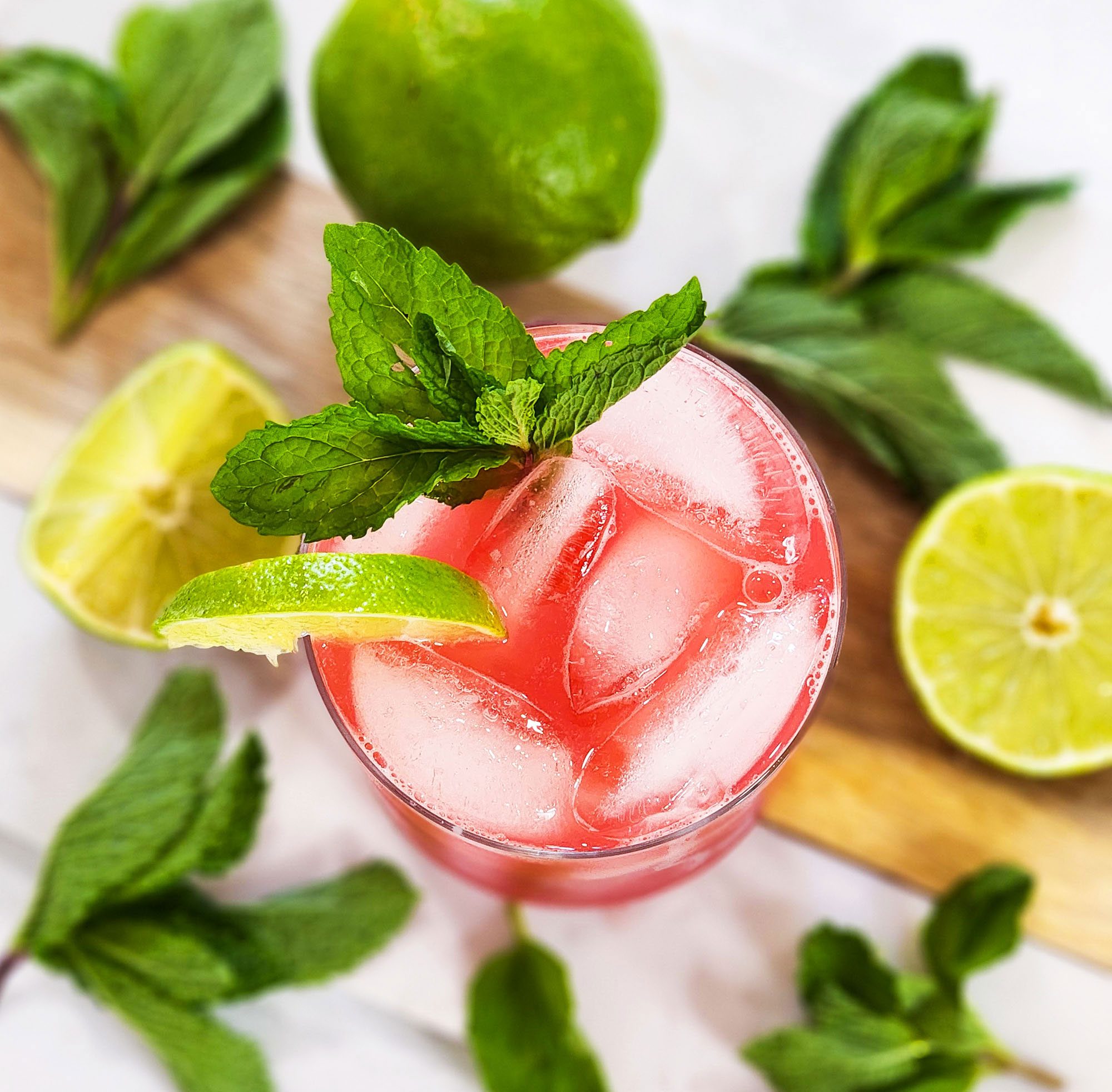 top view of a bright red watermelon agua frescas in a glass, garnished with lime and mint