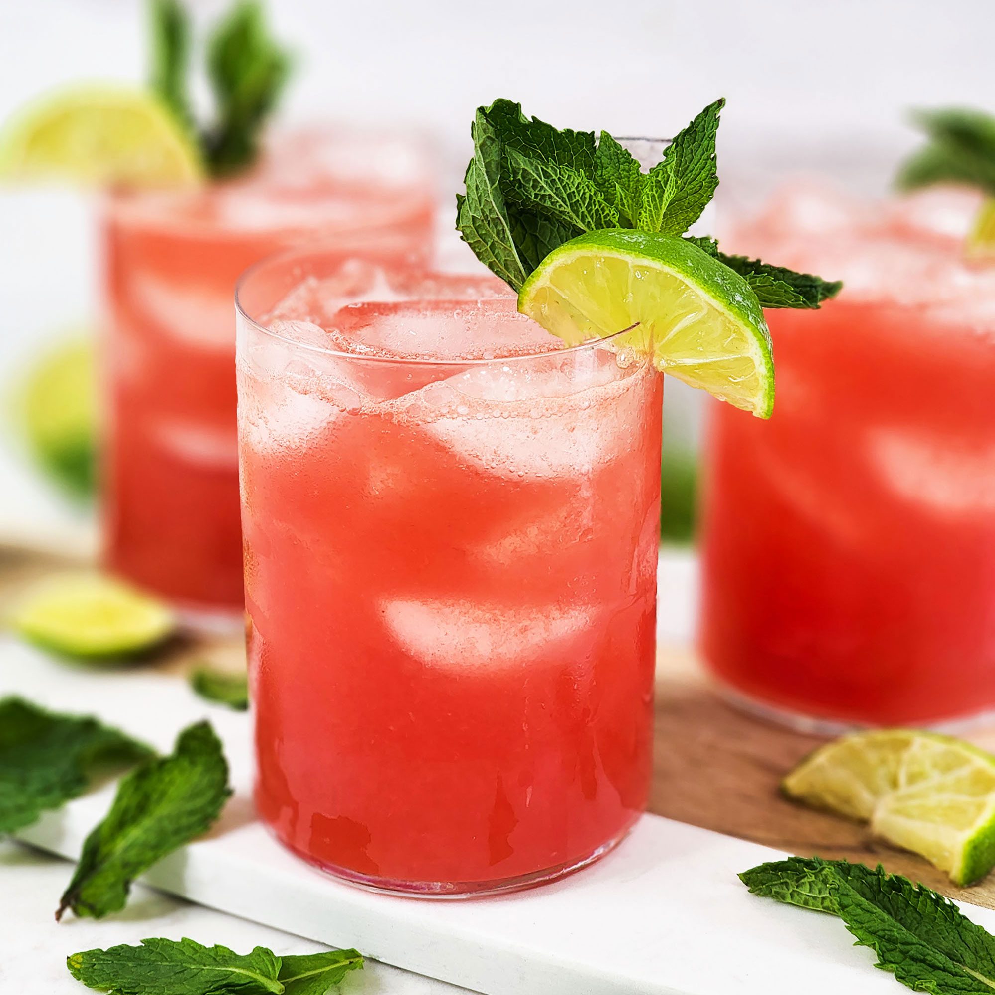 a bright red watermelon agua frescas in a glass, garnished with lime and mint