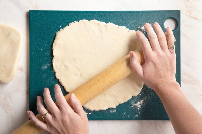 rolling out gluten free pie crust on a teal cutting board