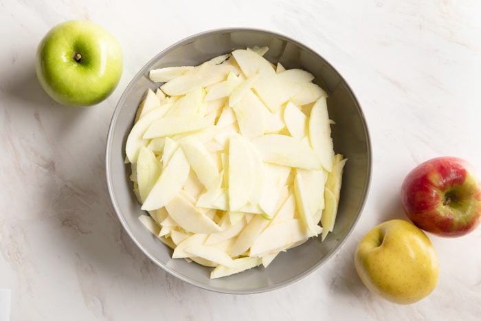 a variety of sliced apples in a bowl with three apples off to the side