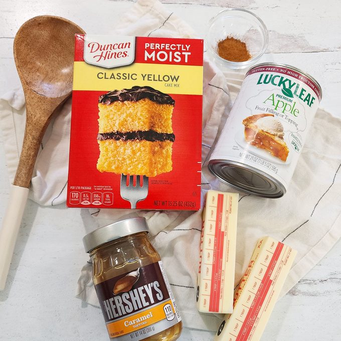 Ingredients For Caramel Apple Dump Cake on a kitchen counter with a wooden spoon, view from above