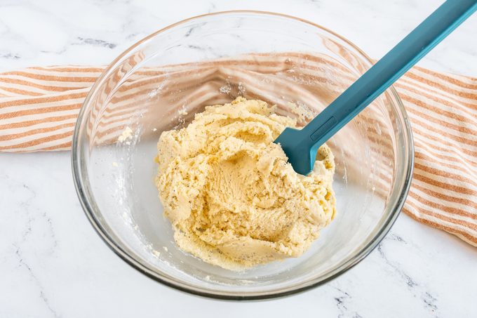 cookie dough in a clear glass bowl with a teal rubber spatula on a kitchen counter