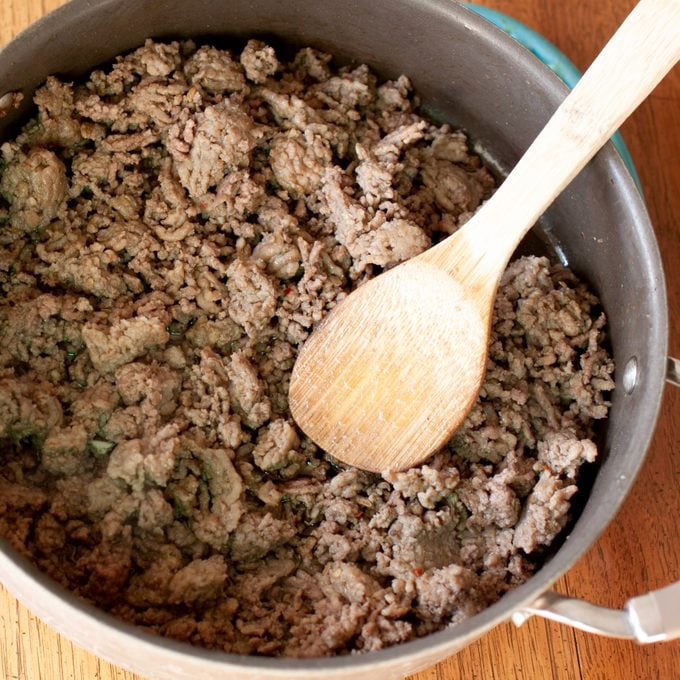 browned beef in a pot with a wooden spoon