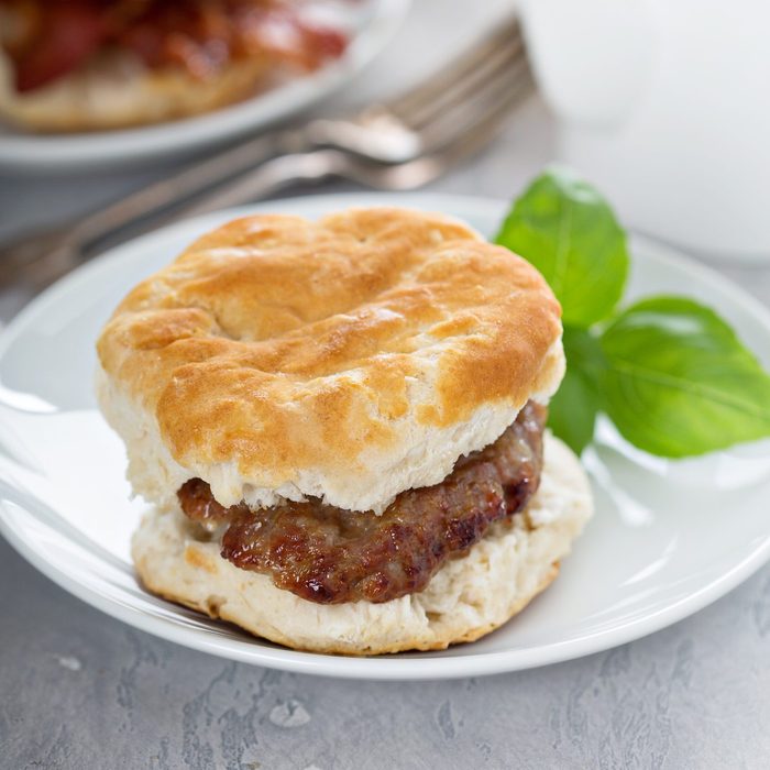 Breakfast biscuits with sausage on a white plate and basil on the side for a garnish