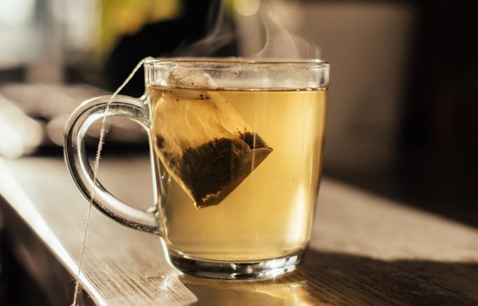 Putting tea bag into glass cup full of hot water