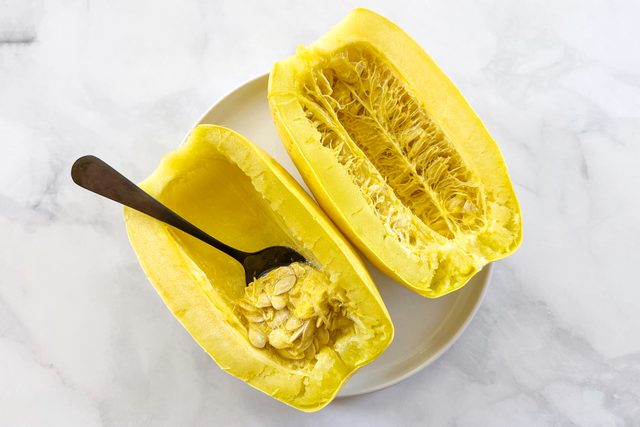 Cooked Microwave Spaghetti Squash with a spoon scooping out the seeds