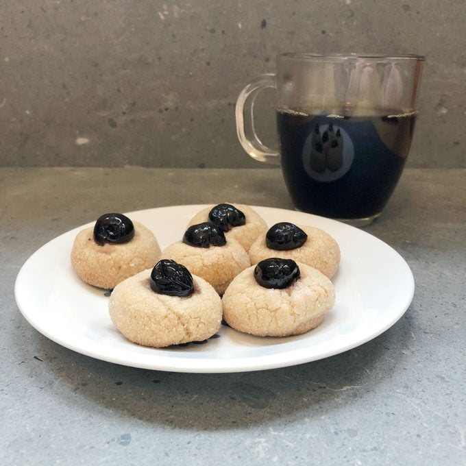a plate of cookies topped with cherries and a cup of coffee in the background