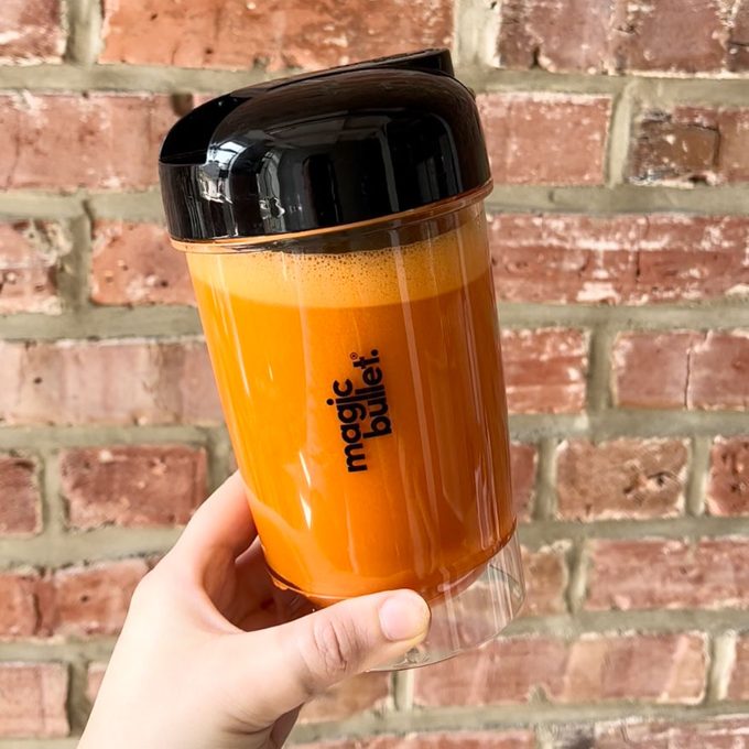 a hand holding magic bullet cup filled with carrot juice