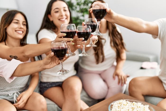 Group of young hispanic women celebrating pajamas party toasting with red wine at home.