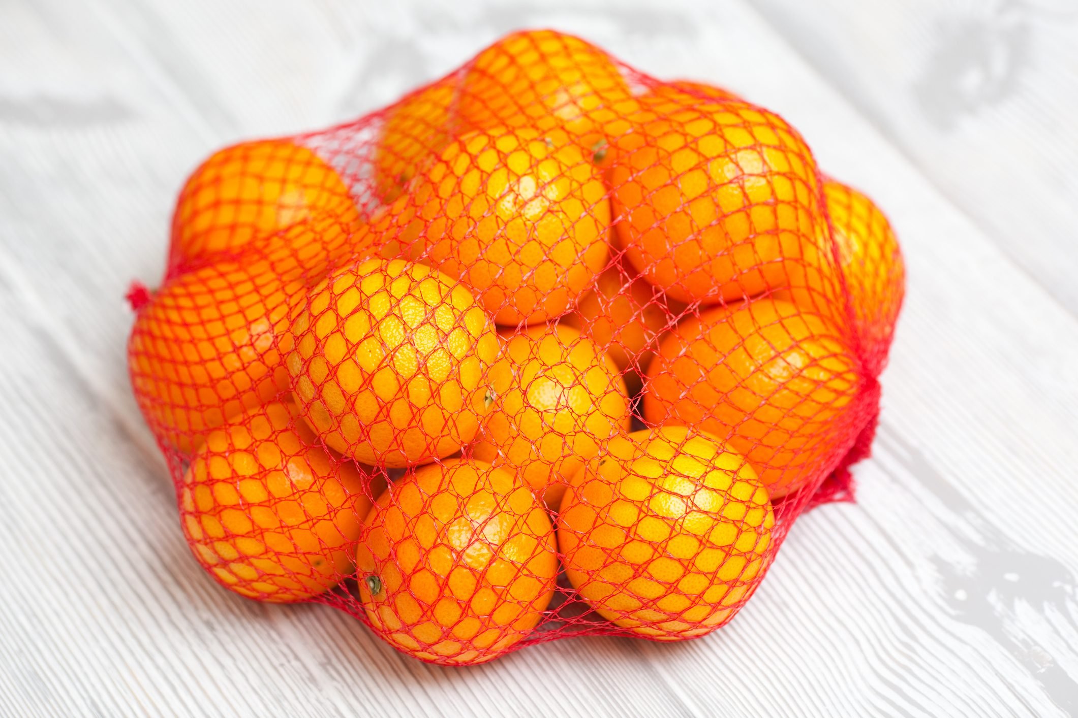 oranges in net bag on white wood background