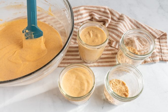 No-Bake Pumpkin Cheesecakes Being Spooned into Mini Jars