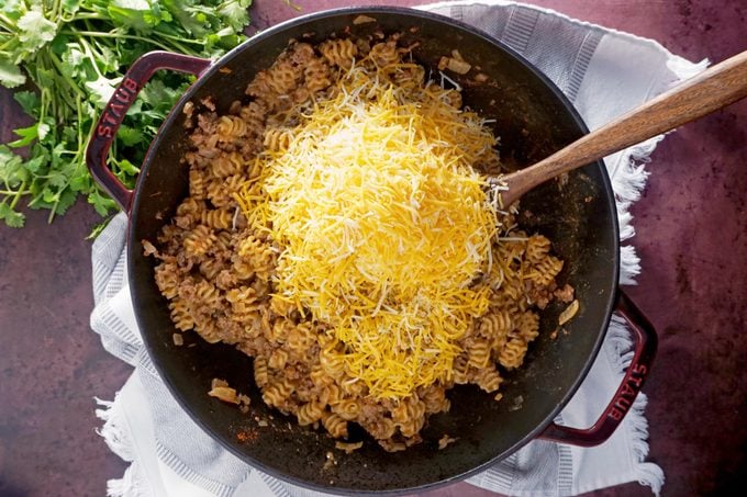 adding cheese to the taco pasta in a pan