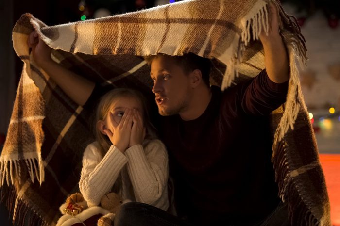 Father telling horror Christmas story for little girl sitting under cozy plaid
