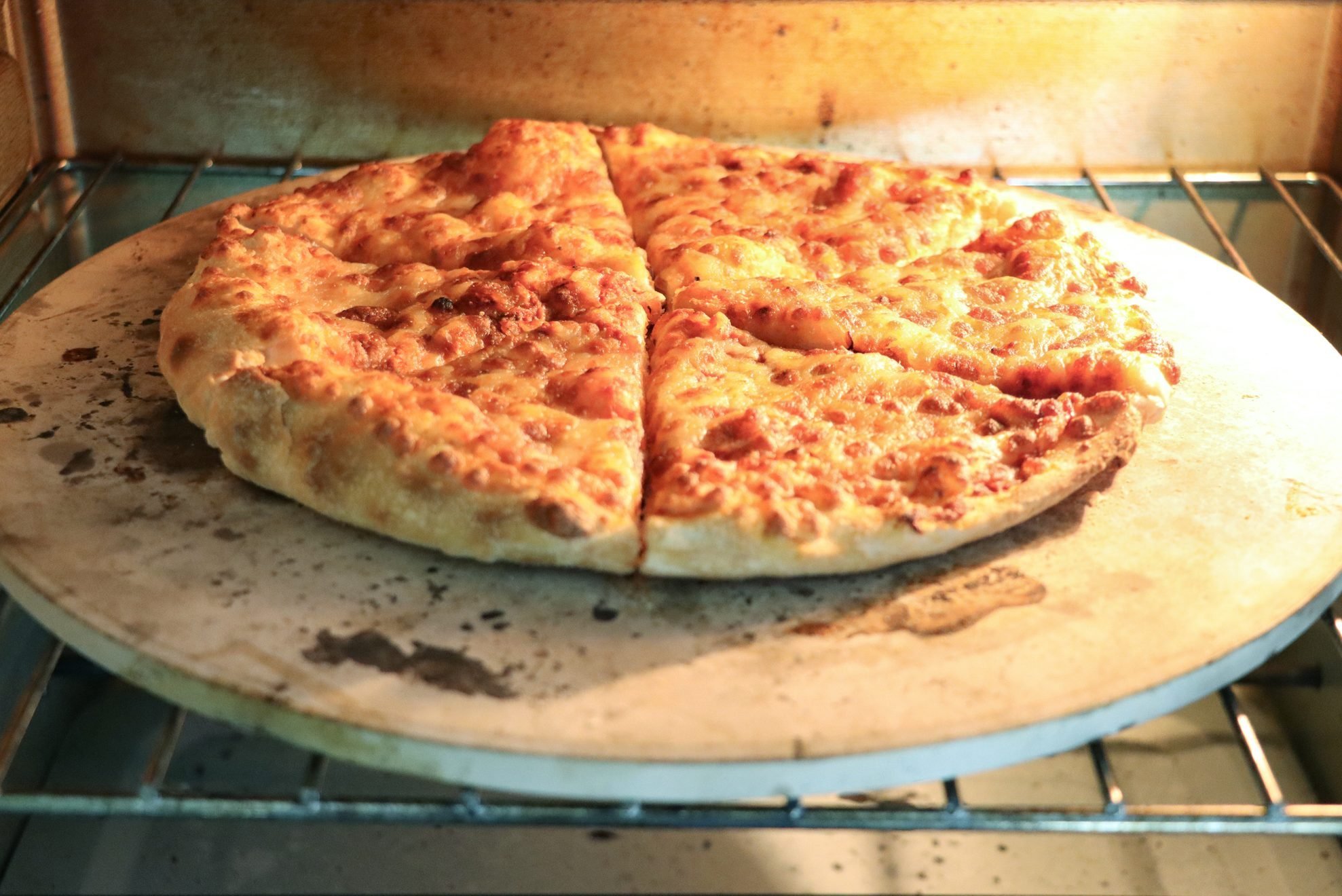 Close-up image of homemade Pizza Margherita baking in oven, cooked on pizza stone for crispy base, grated mozzarella cheese topping, elevated view, focus on foreground