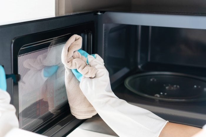 Woman hand with microfiber rag cleaning inside of microwave oven. Closeup