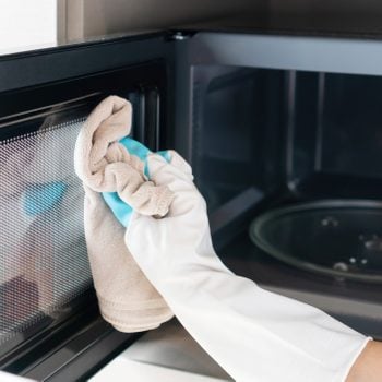 Woman hand with microfiber rag cleaning inside of microwave oven. Closeup