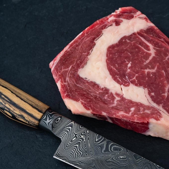 Raw Wagyu Beef Ribeye Steak on a Dark background with a damascus kitchen knife 