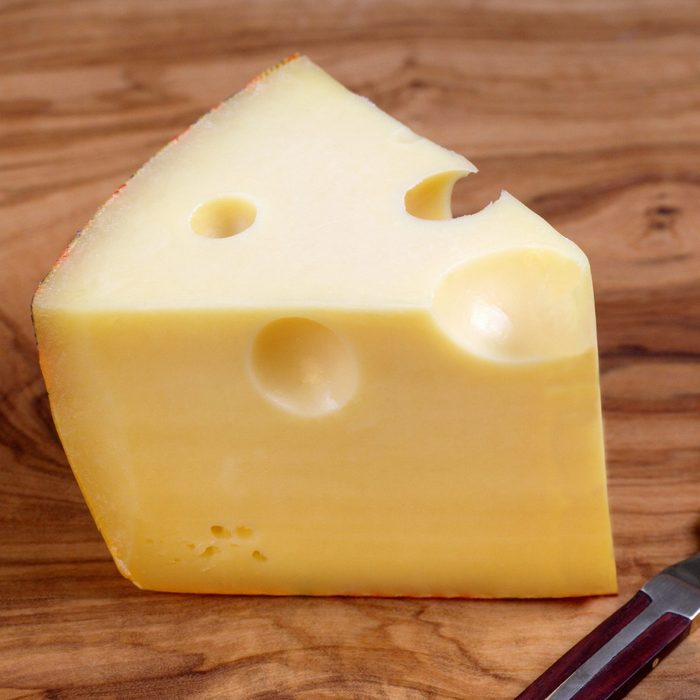 Wedge of gruyere cheese on board, with knife, close-up