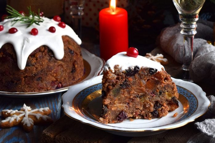 Traditional english steamed pudding with winter berries, dried fruits, nut in festive setting with christmas tree, burning candle and glass of champagne.