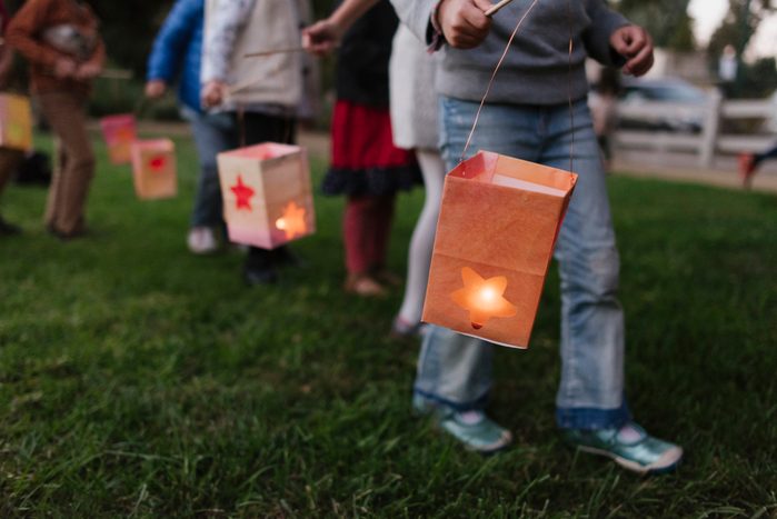 Low section of children carrying illuminated paper lanterns while walking on field