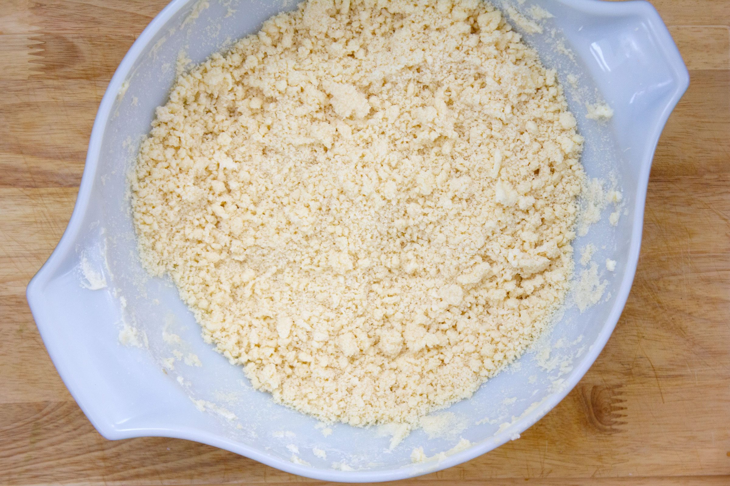 crumbly dough in a plastic bowl on a wooden surface