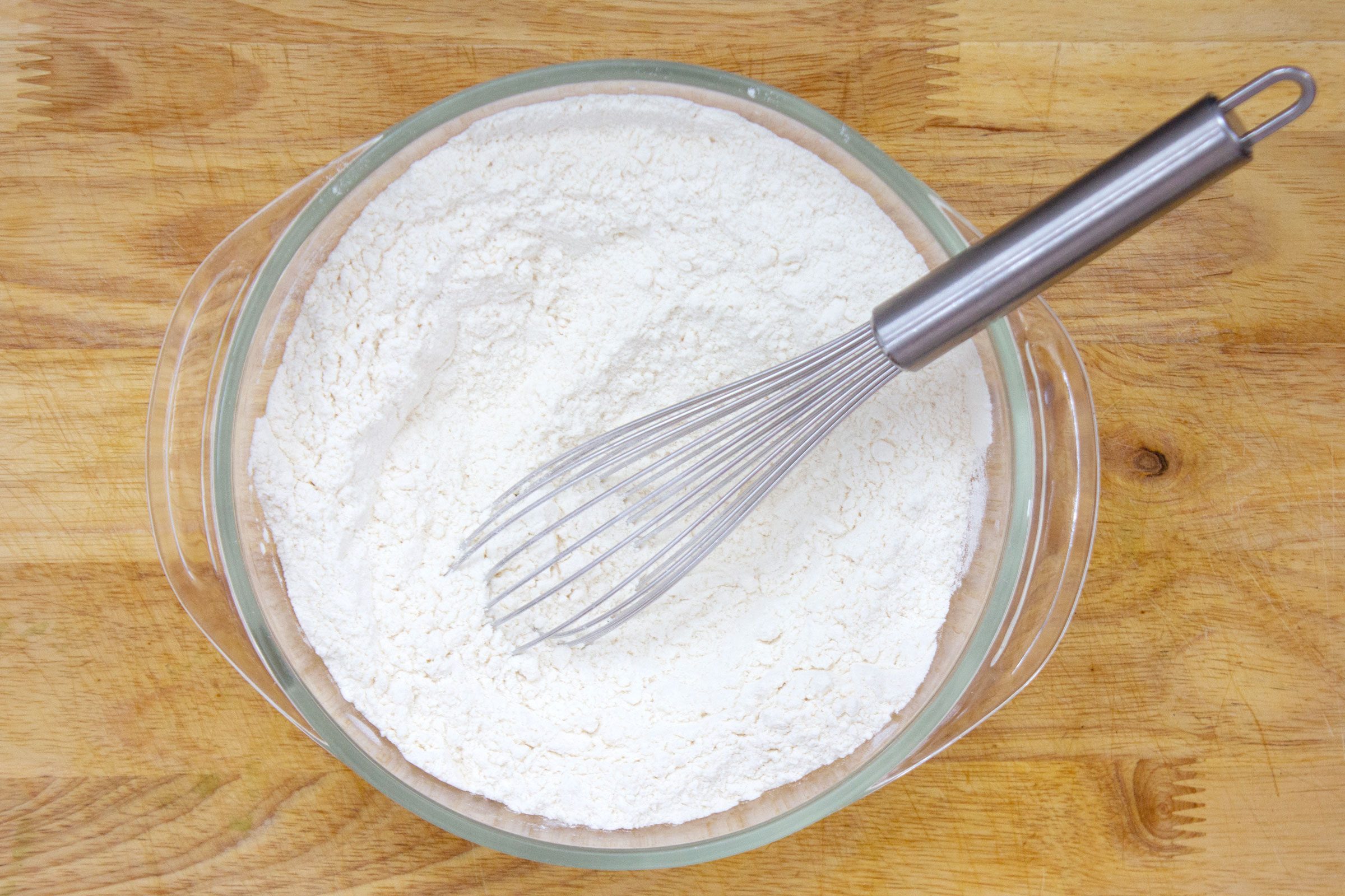 whisking together dry ingredients in a glass bowl on a wooden surface